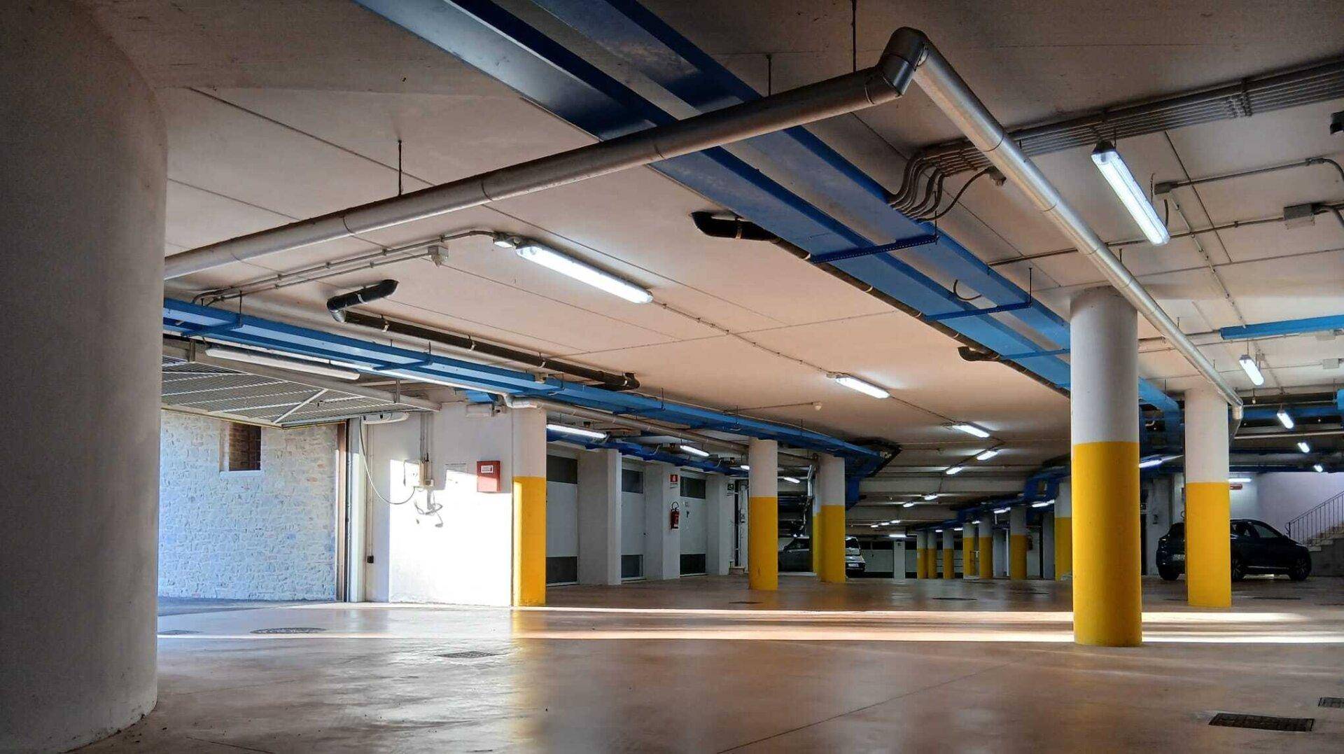 Geräumige Tiefgarage mit Betonboden, gelben Säulen und blauen Leitungen an der Decke.