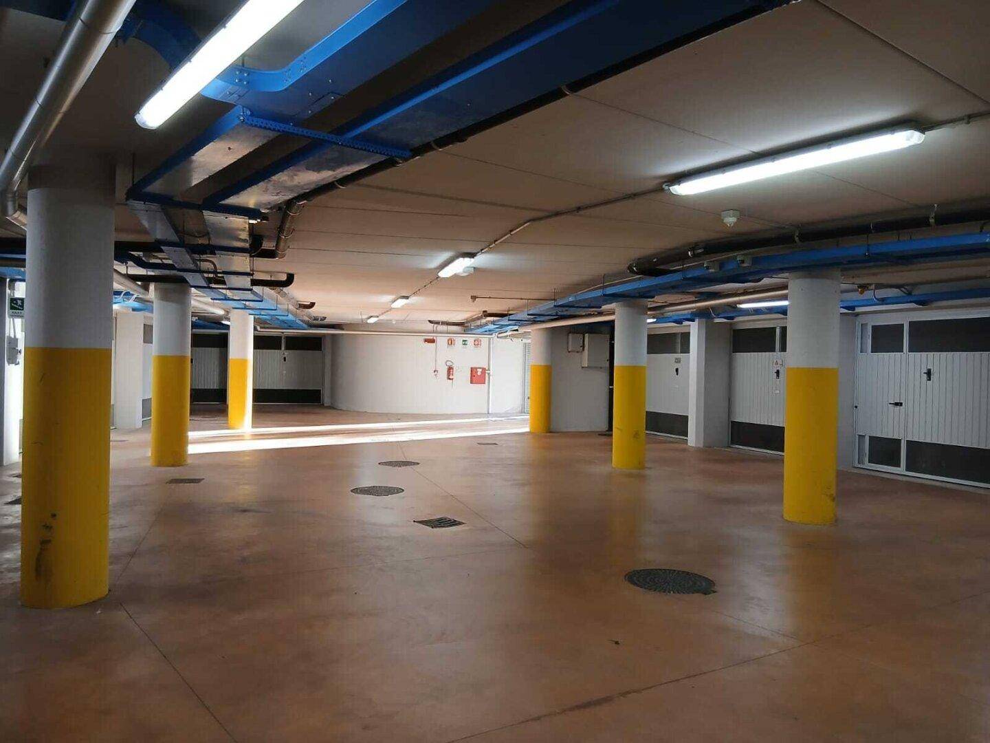 Weitläufige Tiefgarage mit nummerierten Garagenboxen, gelben Säulen und blauen Leitungen.