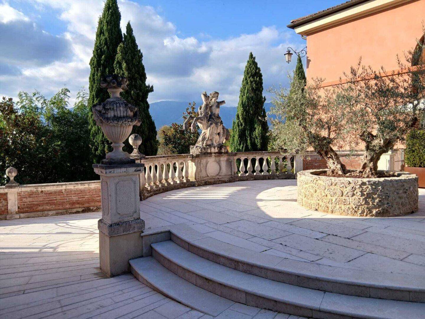 Große, gepflasterte Terrasse mit Balustrade, dekorativen Vasen und Blick auf die Landschaft.
