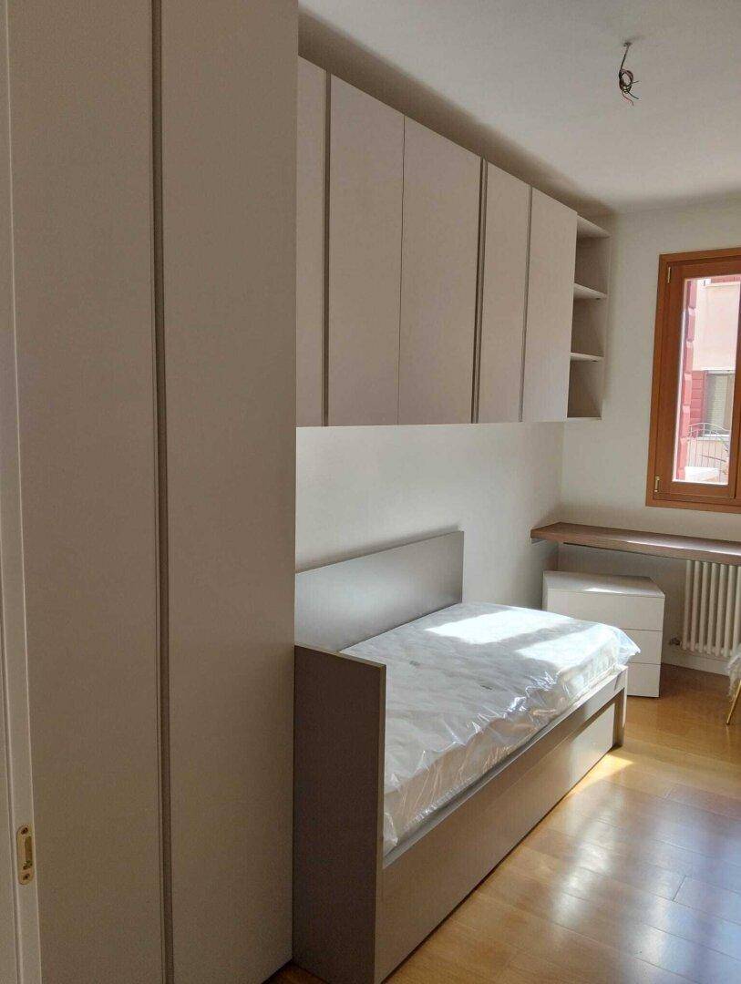 Helles Schlafzimmer mit Einzelbett, integrierten Schränken und Holzfußboden.