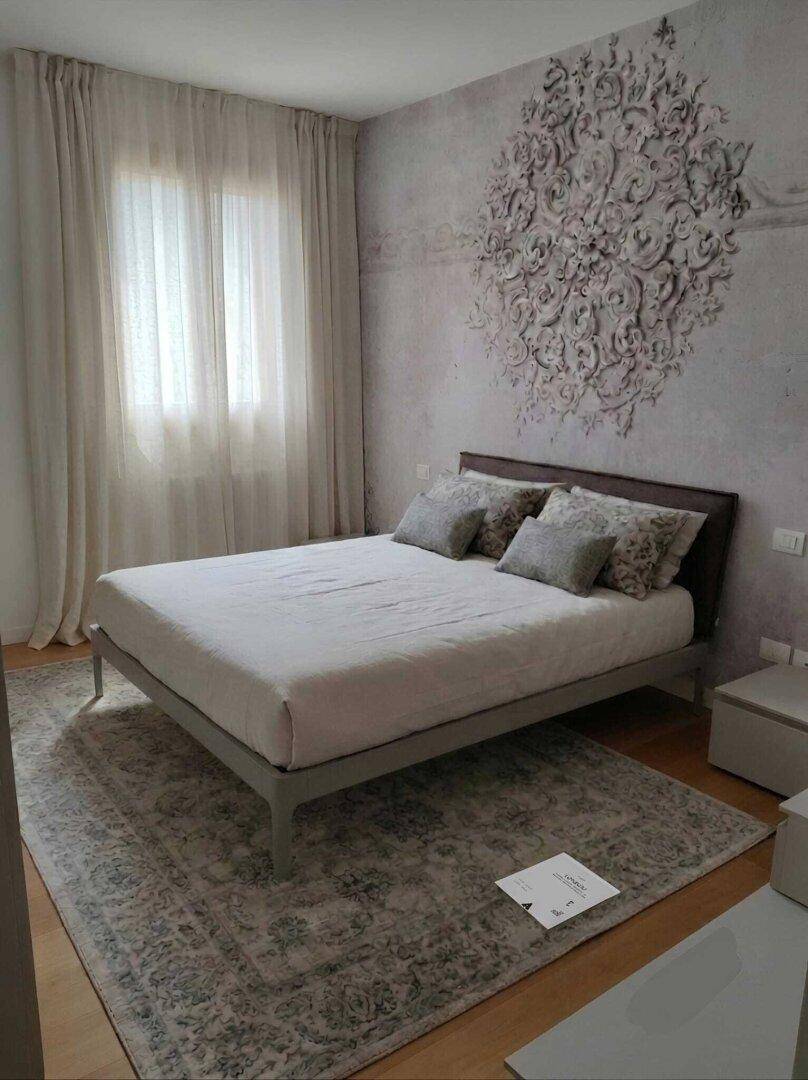 Helles Schlafzimmer mit Doppelbett, dekorativer Wandgestaltung und großem Teppich.