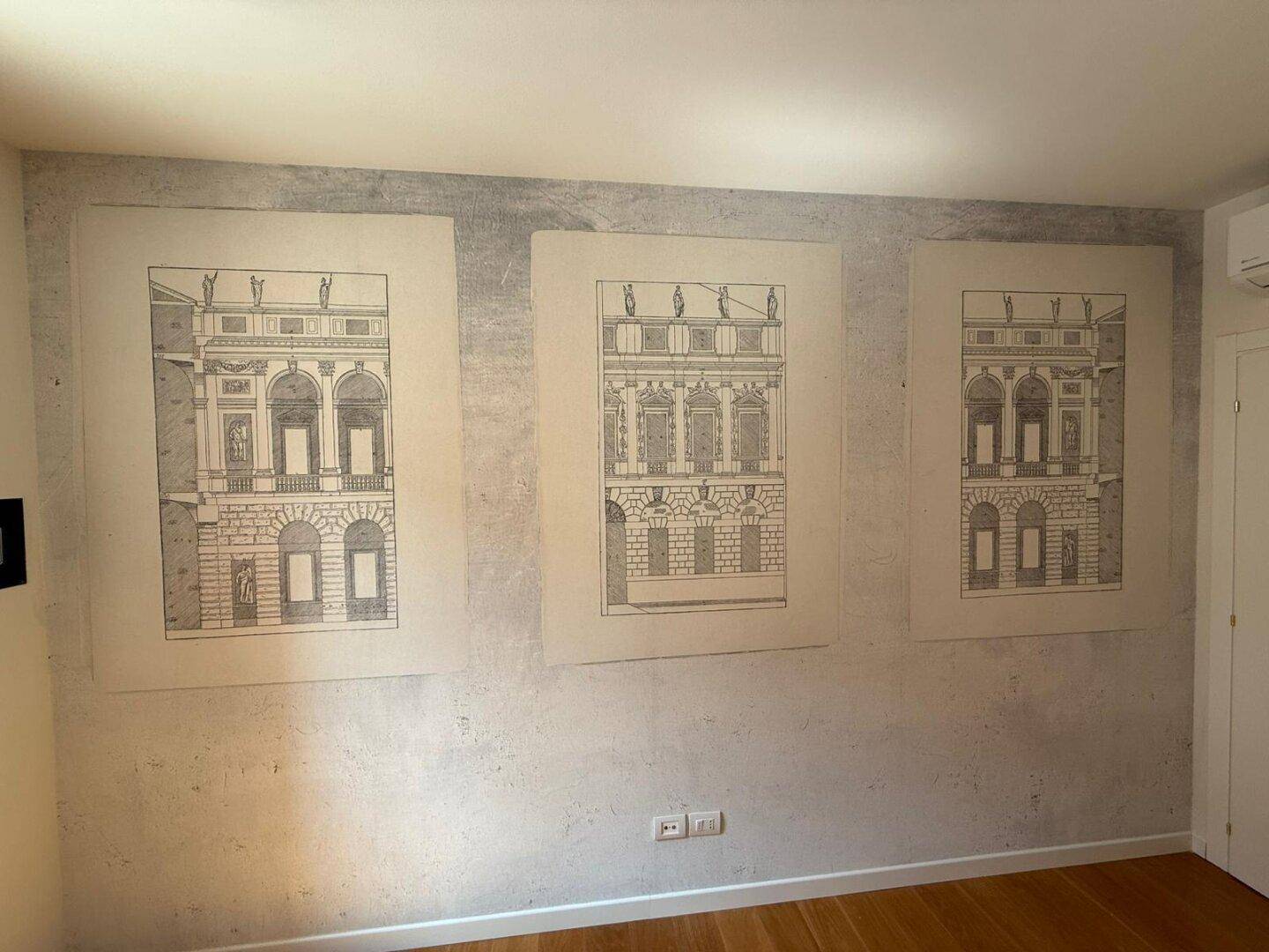 Innenraum mit heller Wand und drei gerahmten architektonischen Zeichnungen als Dekoration.