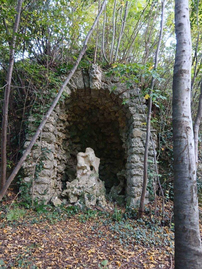 Eine alte Steingrotte mit einer Skulptur in einem bewaldeten Gebiet.