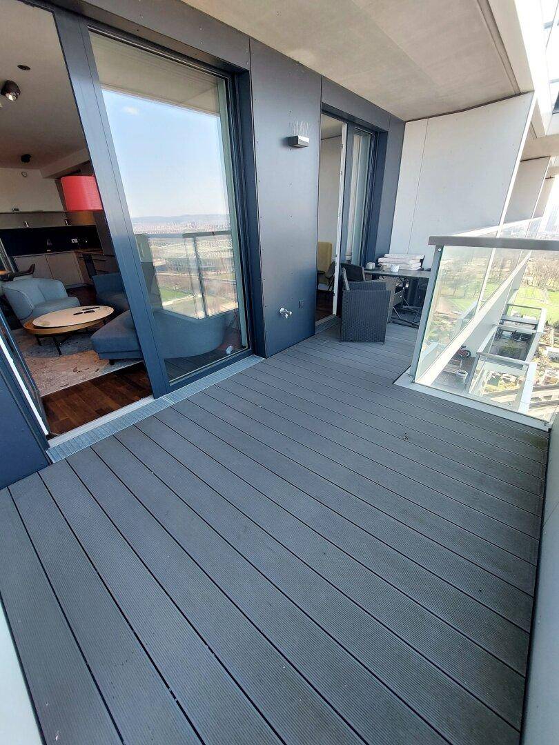 Moderner Balkon mit grauen Dielen, Glasgeländer und Blick auf die Stadt und den Fluss.