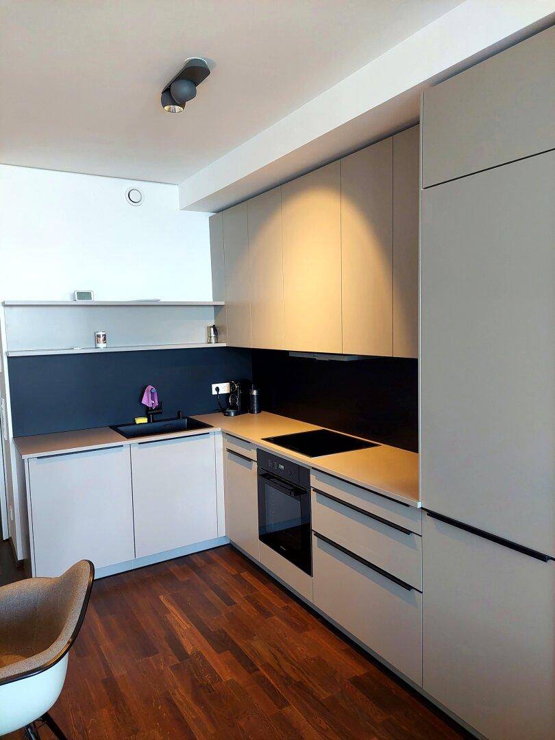 Moderne Einbauküche mit grauen Schränken, schwarzer Rückwand und integrierten Geräten.