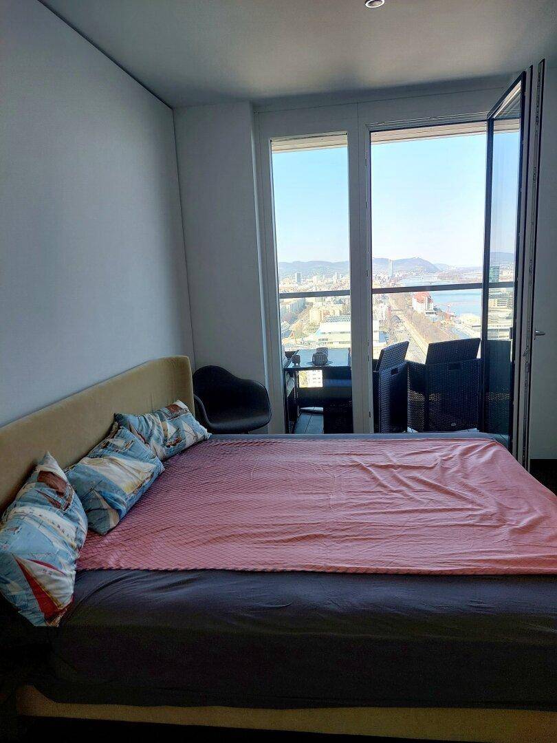 Schlafzimmer mit großem Bett und Zugang zu einem Balkon mit weitem Stadt- und Flussblick.