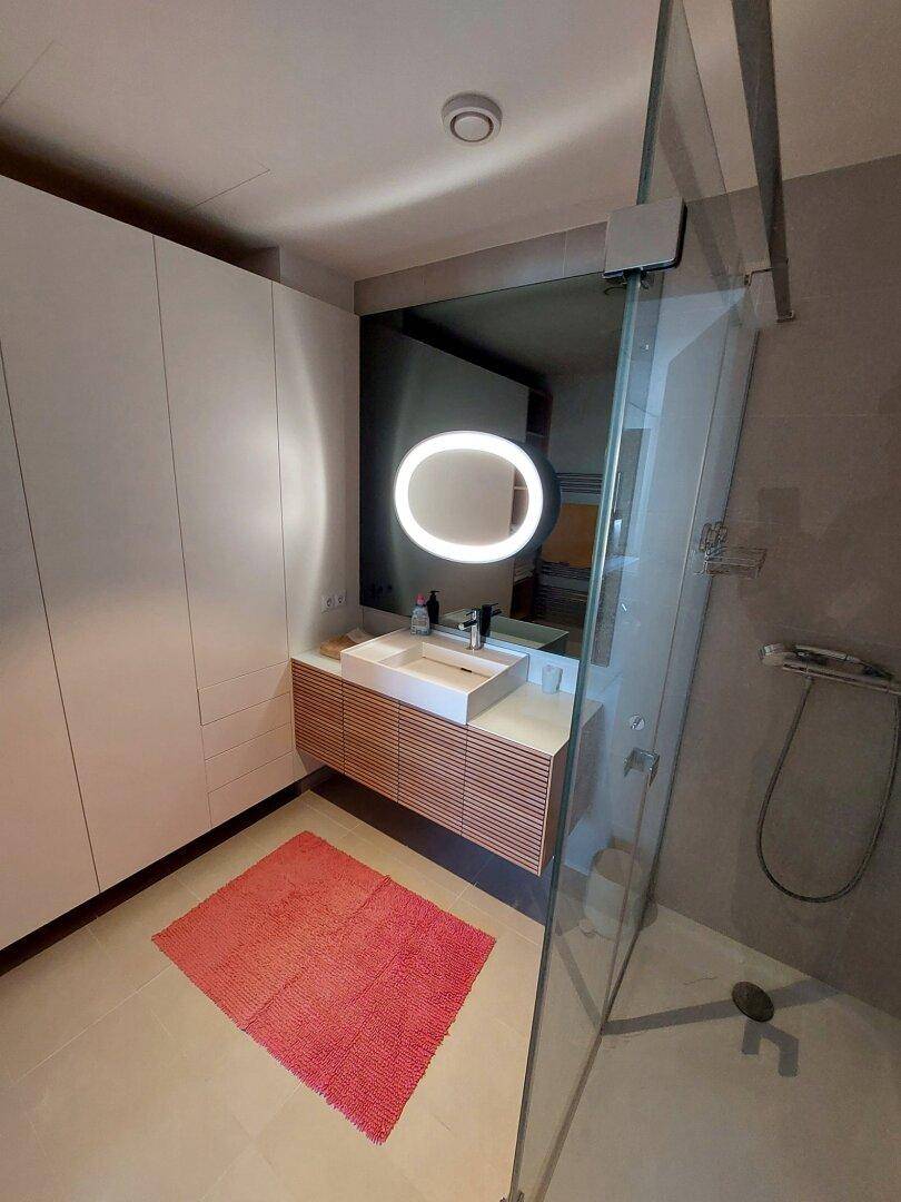 Modernes Badezimmer mit schwebendem Waschtisch, beleuchtetem Spiegel und begehbarer Dusche.