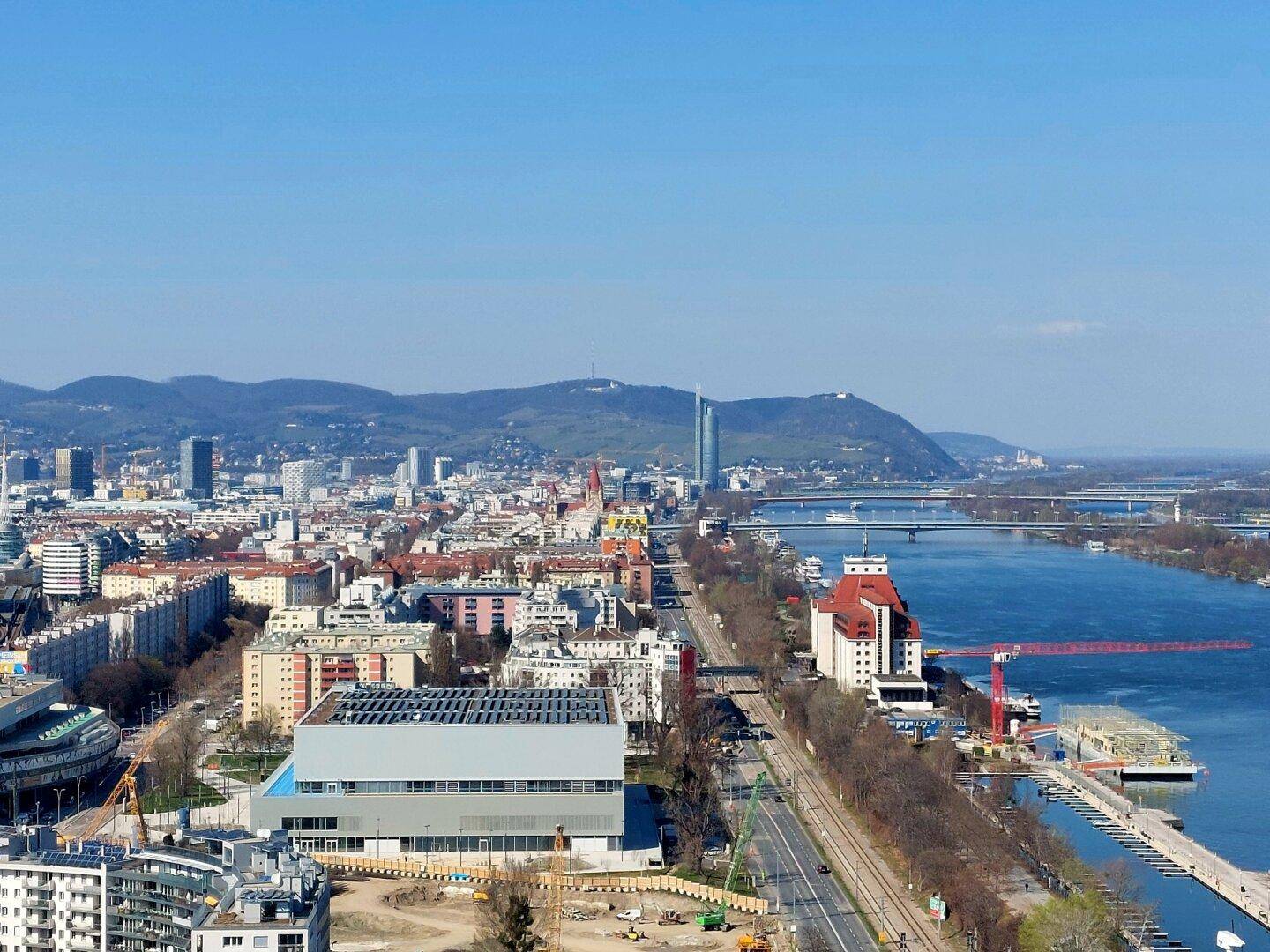 Panoramablick auf die Donau, die Wiener Skyline und die umliegende Berglandschaft.