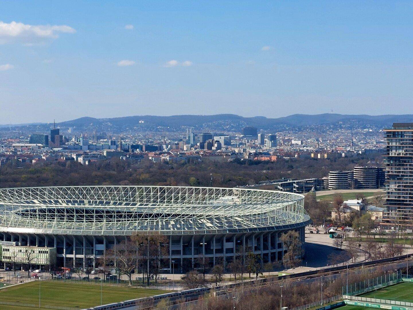 Luftaufnahme des großen Stadions mit der Wiener Skyline und den Hügeln im Hintergrund.