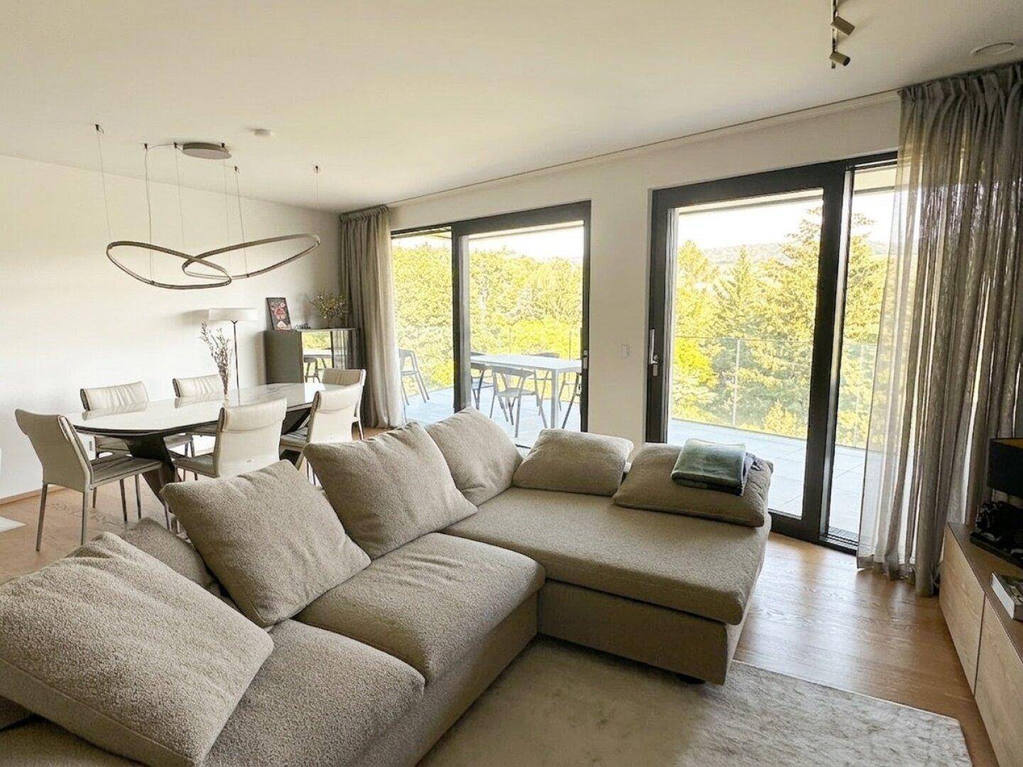 Heller Wohn-Essbereich mit großem Sofa, modernem Esstisch und Zugang zur Terrasse mit Weitblick.