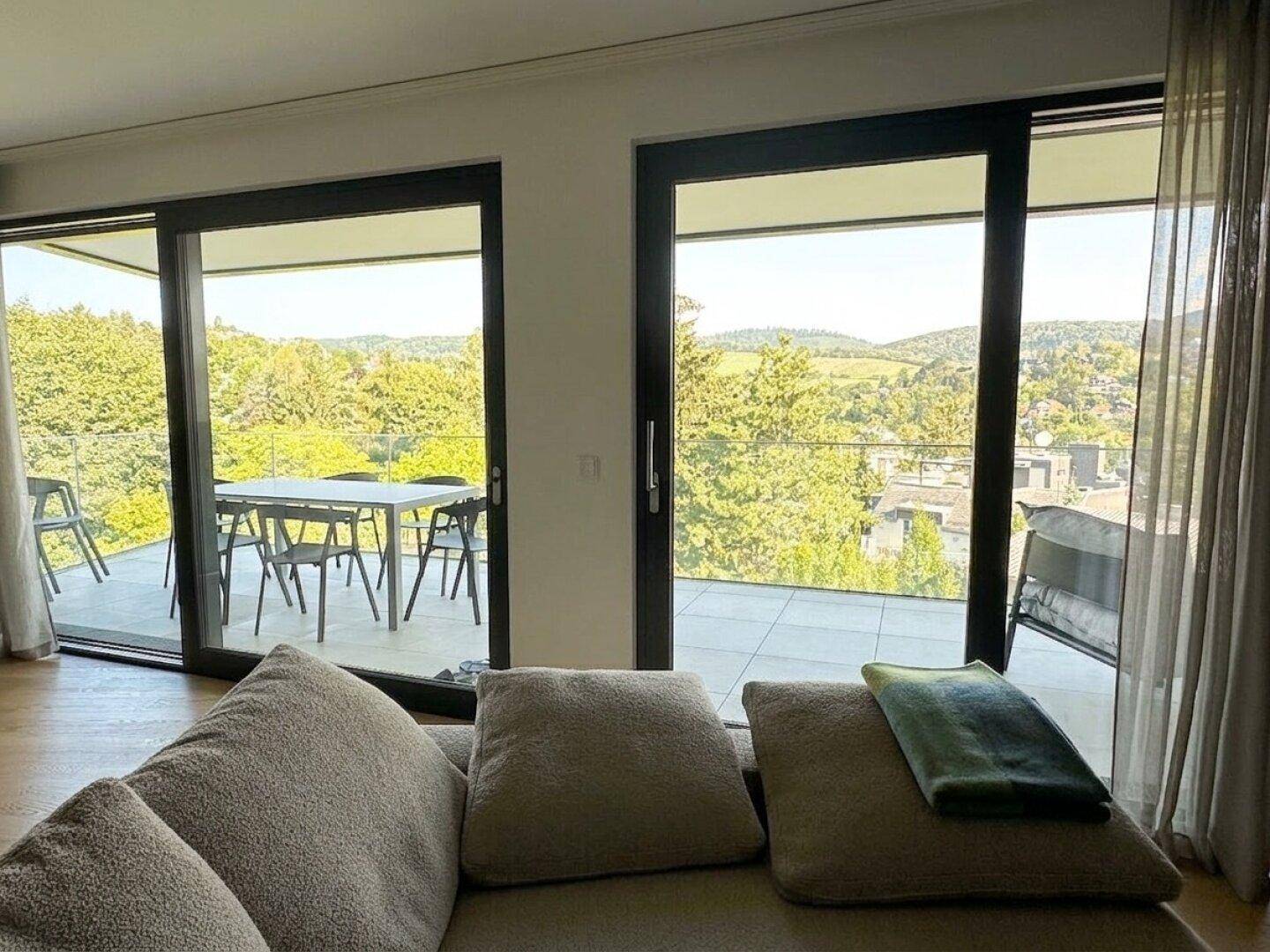 Gemütlicher Wohnbereich mit Blick auf die Terrasse und die grüne Hügellandschaft durch große Fenster.