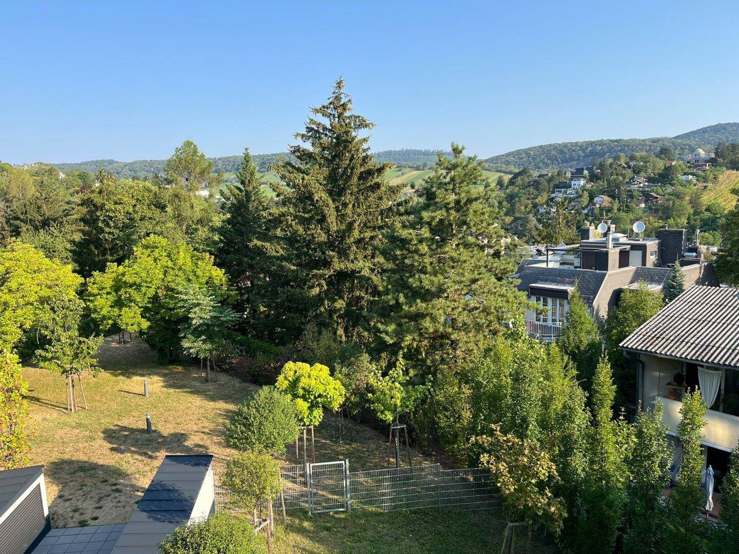 Panoramablick auf eine weitläufige grüne Gartenlandschaft mit Bäumen und umliegenden Häusern.