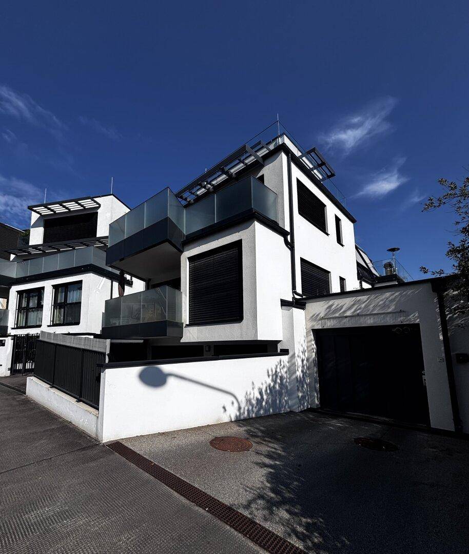 Moderne Architektur des Gebäudes mit weißen Fassaden, dunklen Akzenten und Garagenzufahrt.