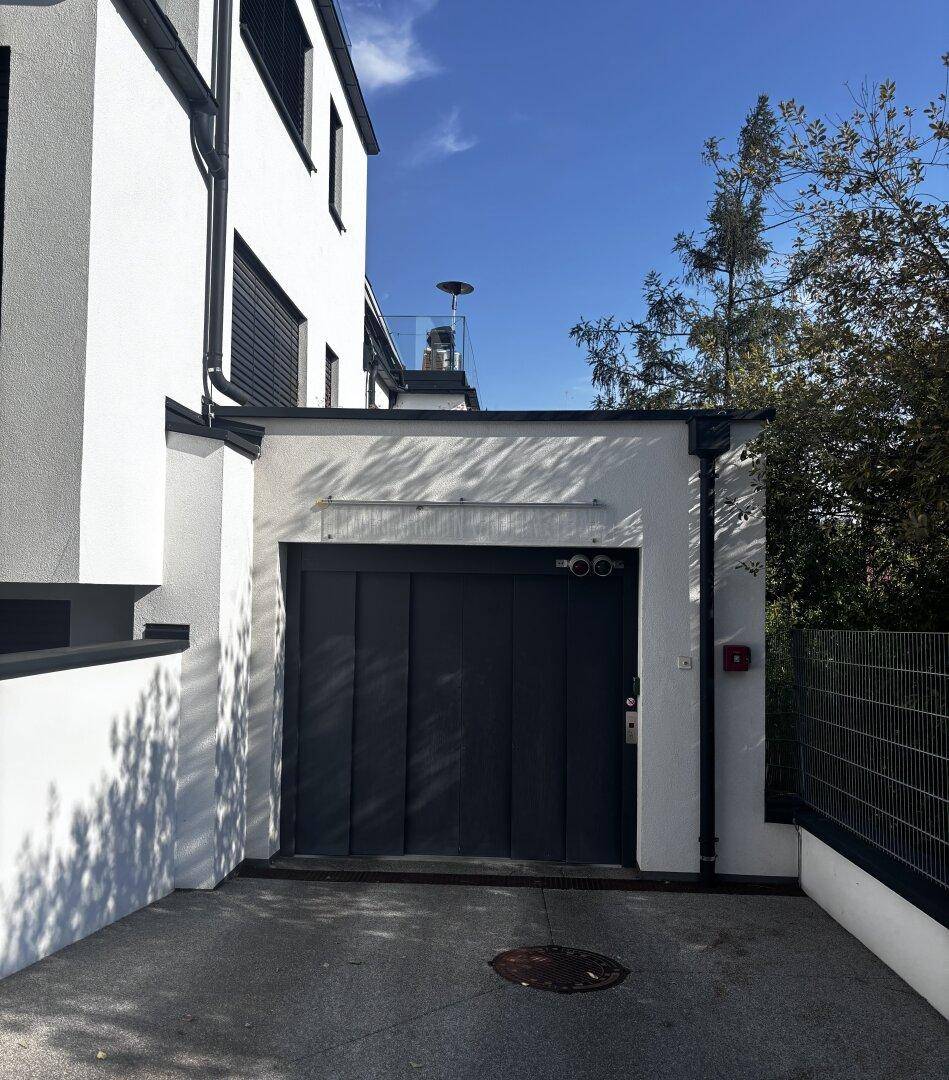 Moderne Gebäudefassade mit integrierter Garageneinfahrt und klaren Linien unter blauem Himmel.