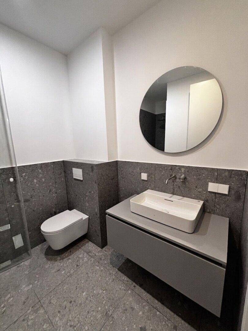 Modernes Badezimmer mit grauen Fliesen, wandhängendem WC und stilvollem Waschtisch.
