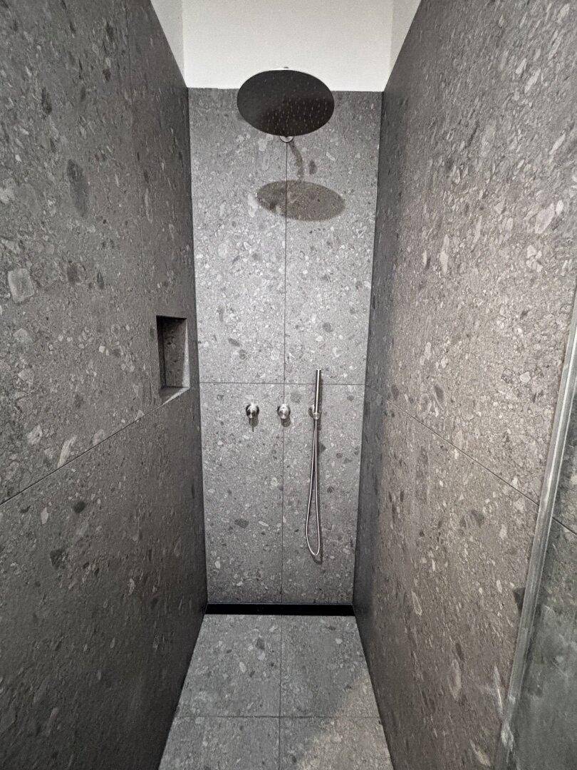 Geräumige Duschkabine mit modernen grauen Fliesen und einer luxuriösen Regendusche.