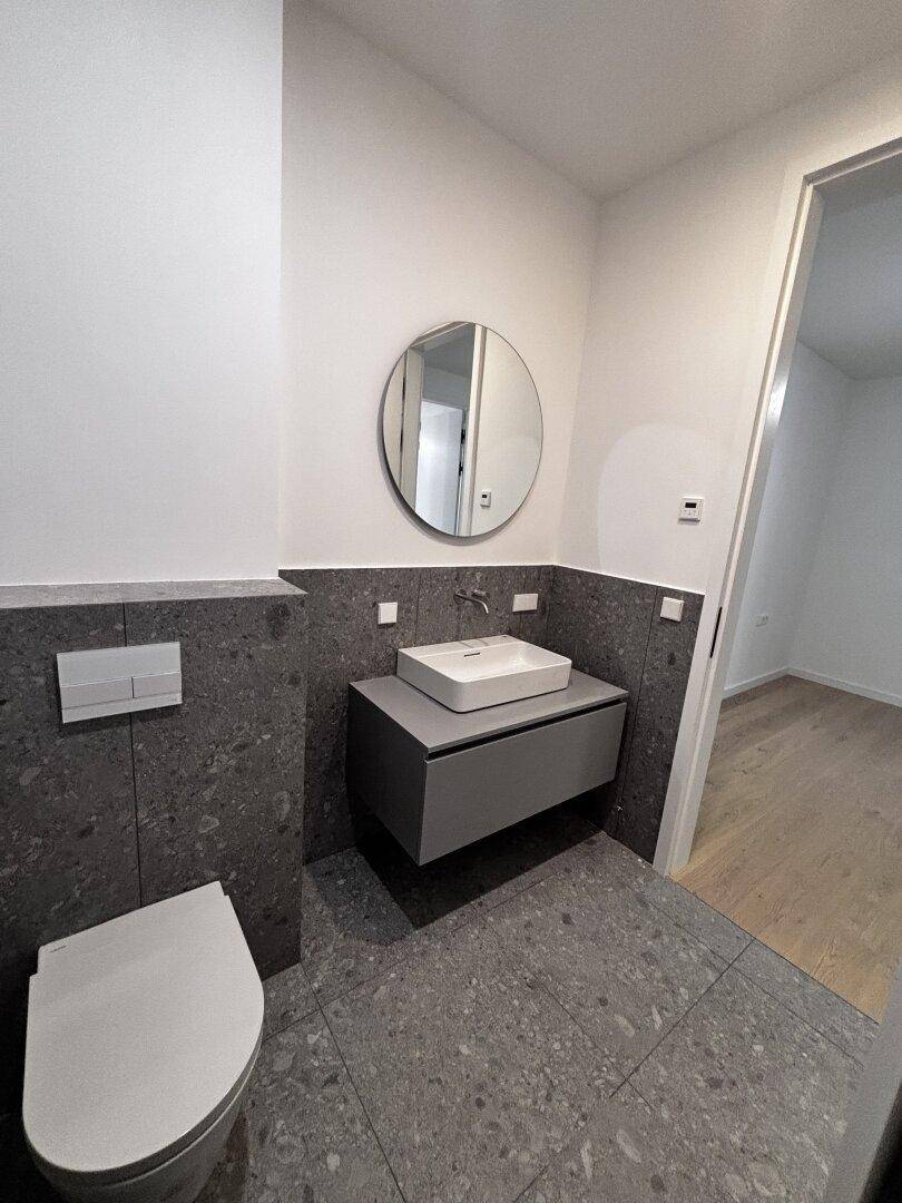Stilvolles Badezimmer mit grauen Fliesen, wandhängendem WC und modernem Waschtisch.