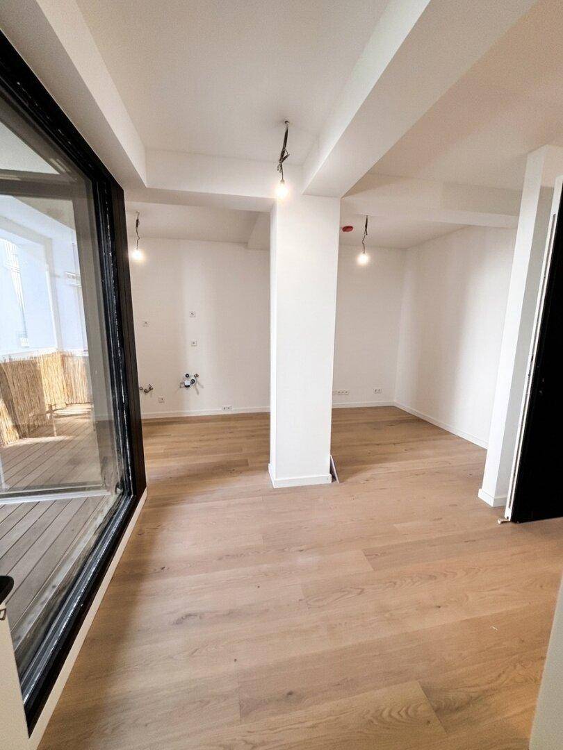 Offener Wohnbereich mit hellem Holzboden, weißen Wänden und großen Fenstern.