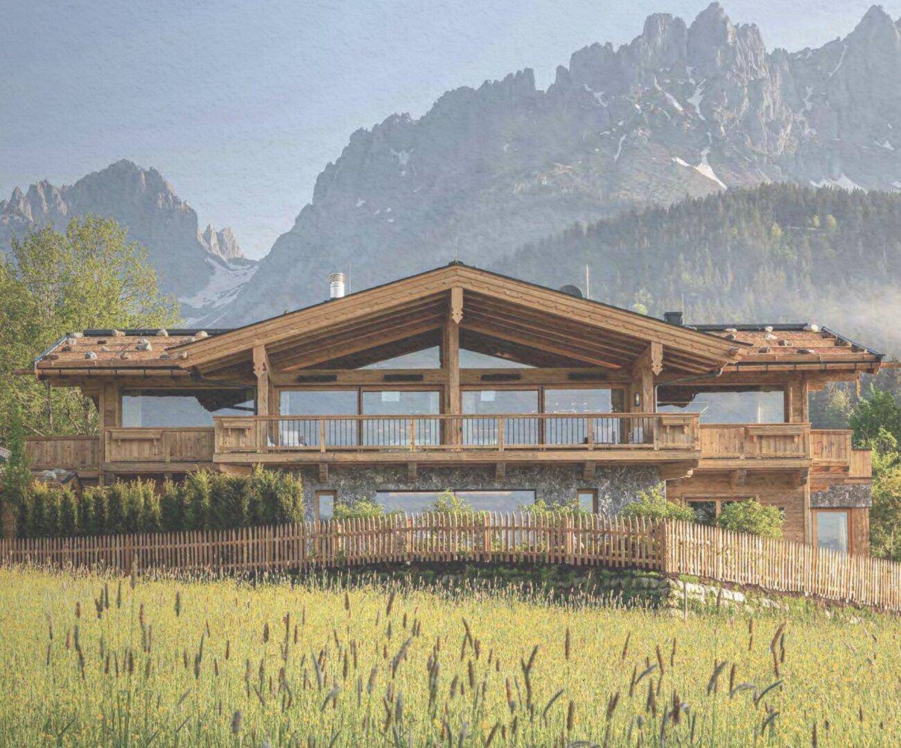 Luxuriöses Holzchalet mit Steinsockel und weitläufigem Gartenbereich vor alpiner Bergkulisse.