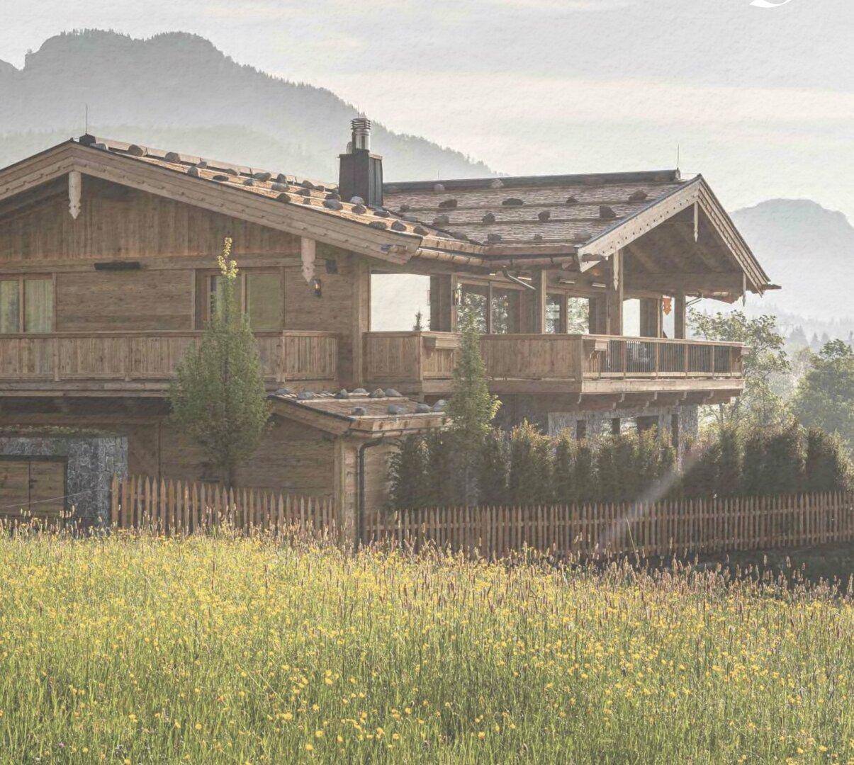 Charmantes Holzchalet mit traditionellem Dach und Balkonen, umgeben von blühenden Wiesen.