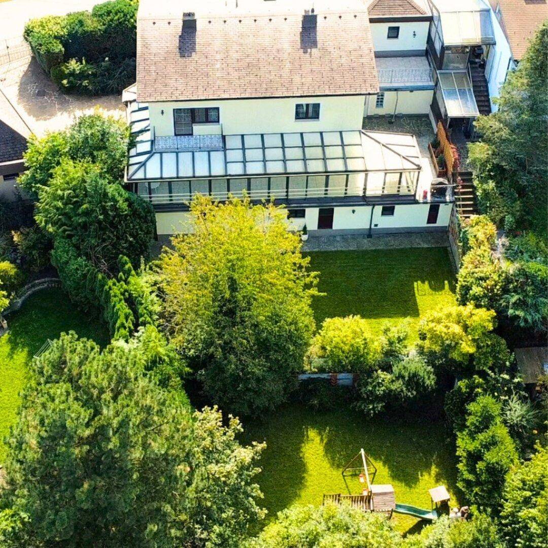Luftaufnahme des Hauses mit weitläufigem Garten, altem Baumbestand und einem kleinen Kinderspielplatz.