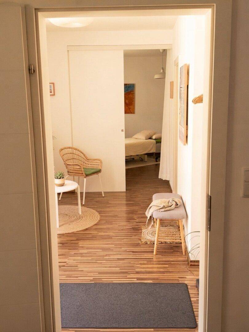 Heller Flur mit Holzboden und Blick in einen gemütlichen Wohnbereich mit Rattan-Sessel.