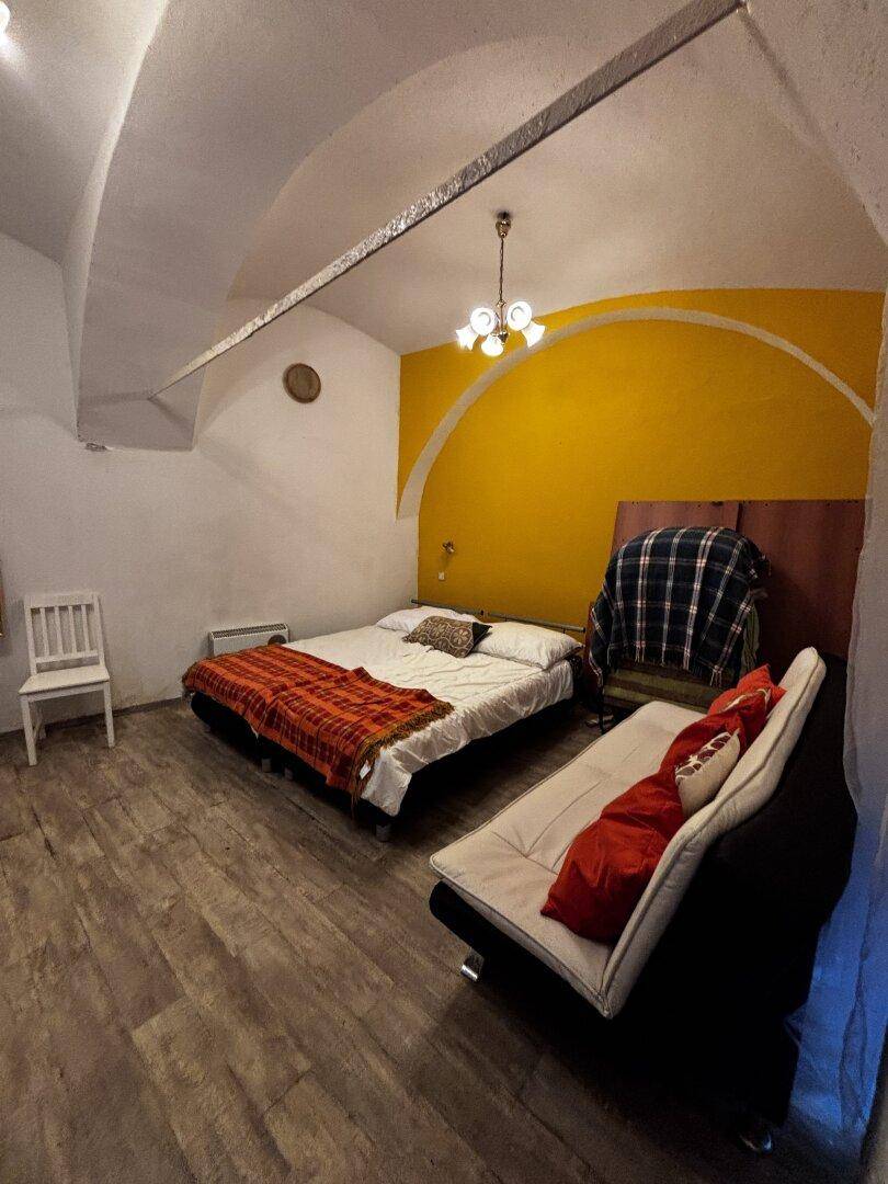 Schlafzimmer mit Doppelbett, Sofa und einer gelben Akzentwand unter gewölbter Decke.