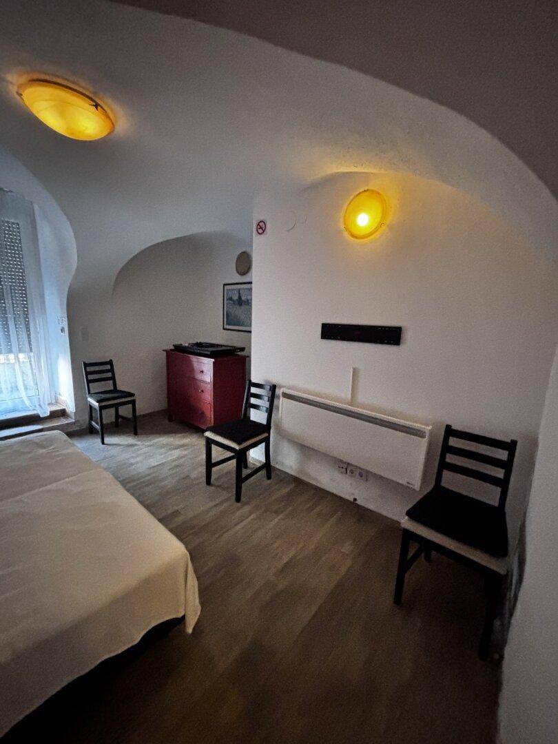 Schlafzimmer mit Einzelbett, Stühlen, roter Kommode und gewölbter Decke, Fenster mit Rollladen.