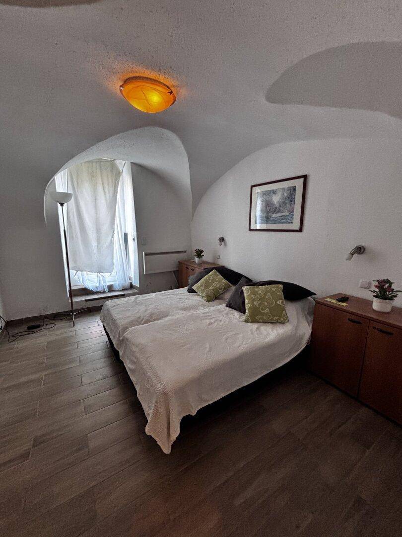 Schlafzimmer mit zwei Einzelbetten, Nachttischen und gewölbter Decke, hell durch das Fenster.