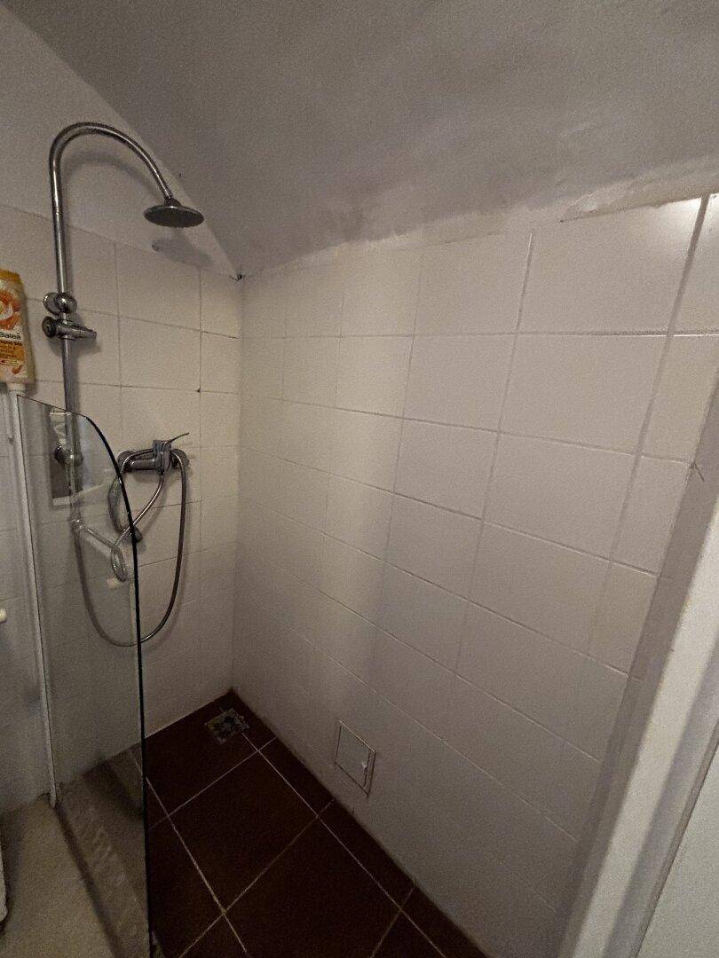 Duschbereich mit weißen Wandfliesen und dunklem Fliesenboden, einfache Ausstattung.