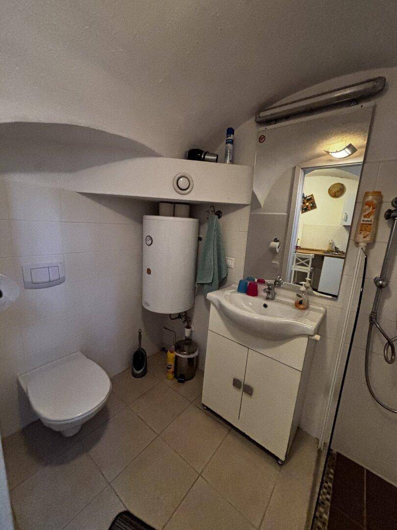Funktionales Badezimmer mit Toilette, Waschbecken, Spiegel und Warmwasserbereiter.