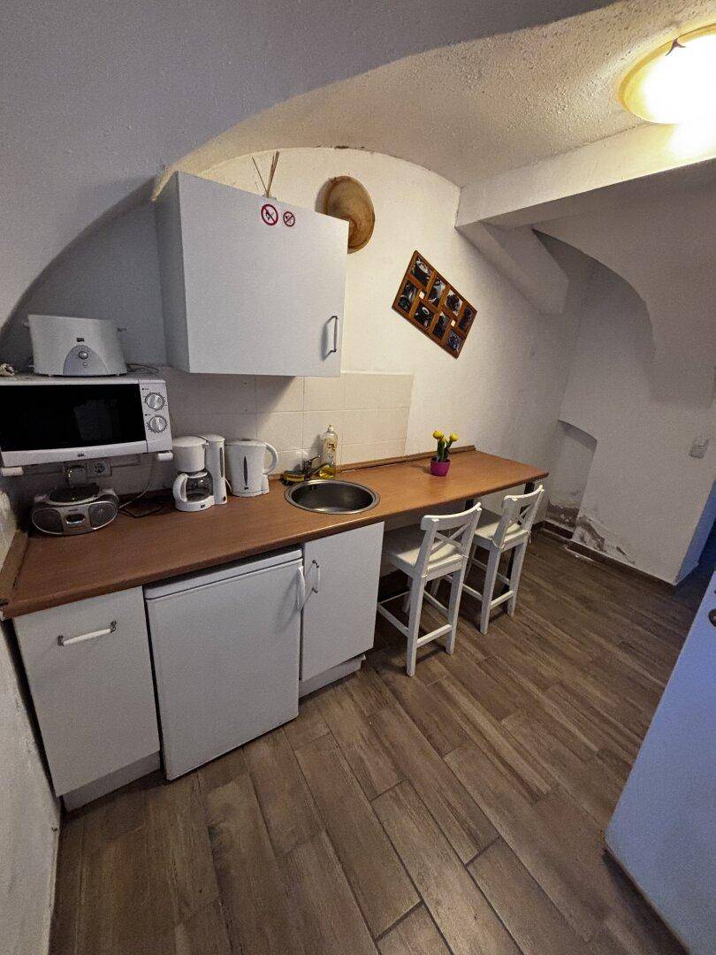 Kleine Küchenzeile mit Holztheke, Spüle, Mikrowelle und zwei Barhockern unter einem Gewölbedach.