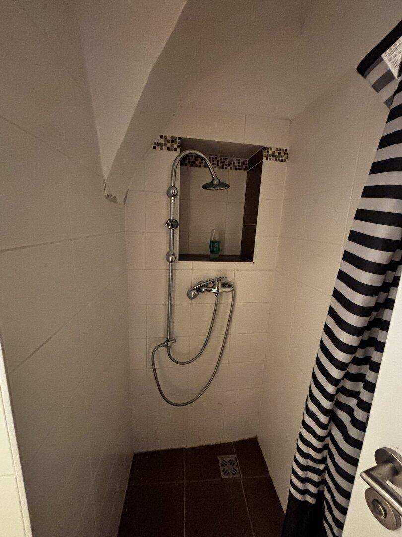 Duschbereich mit Duschkopf und gestreiftem Vorhang in einem gefliesten Raum.
