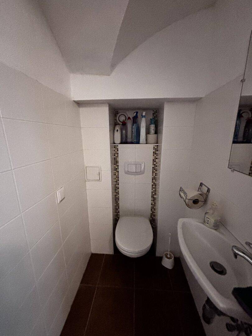 Kleines Badezimmer mit WC, Waschbecken und weißen Fliesen an den Wänden.