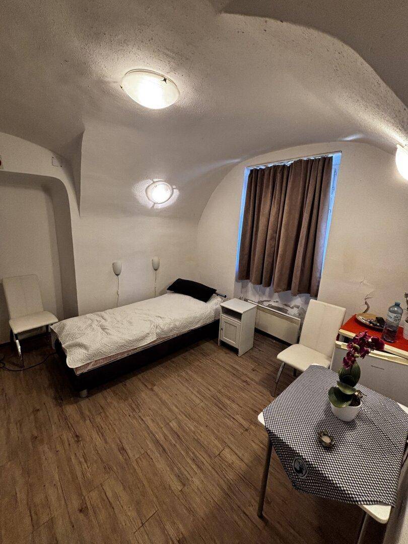 Schlafzimmer mit Einzelbett, Nachttisch, Stühlen und gewölbter Decke, dunkle Vorhänge.