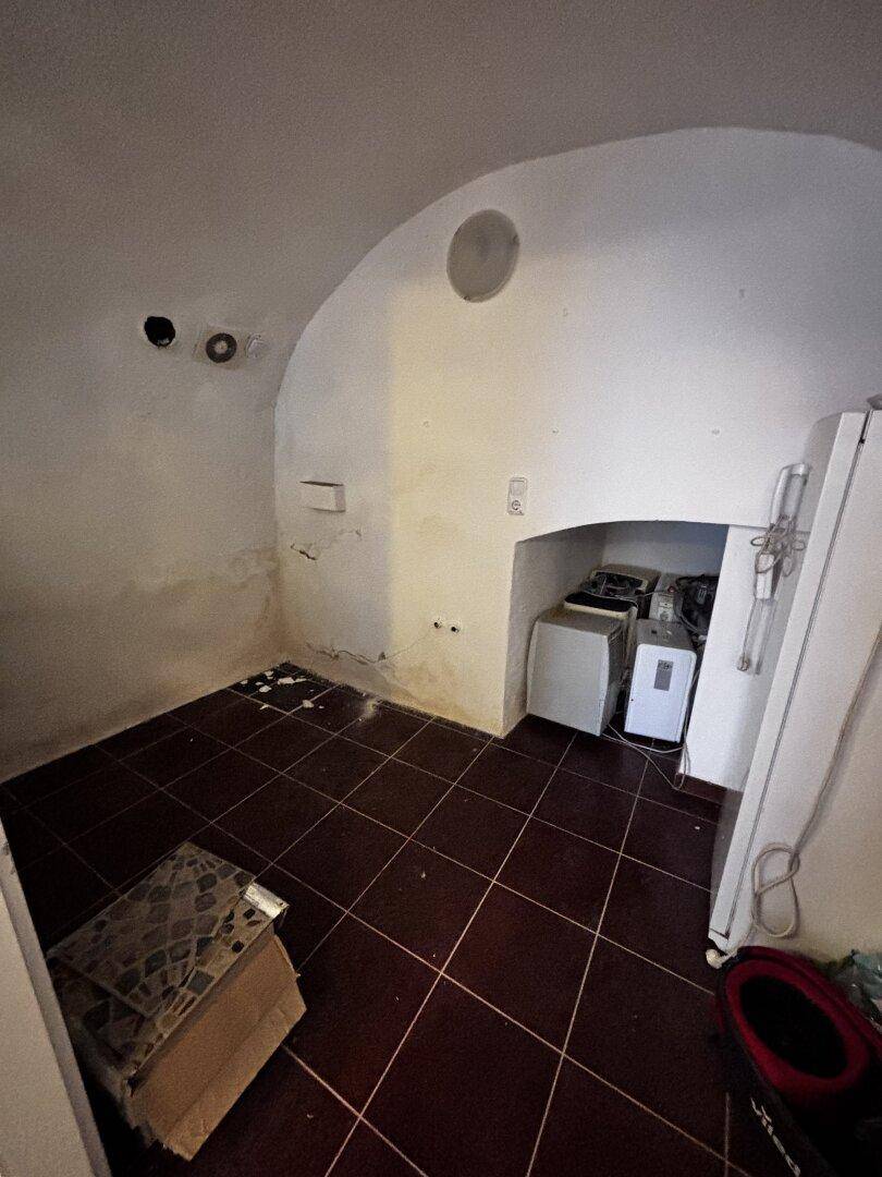 Leerer Raum mit Fliesenboden, gewölbter Decke und Anzeichen von Feuchtigkeit an den Wänden.