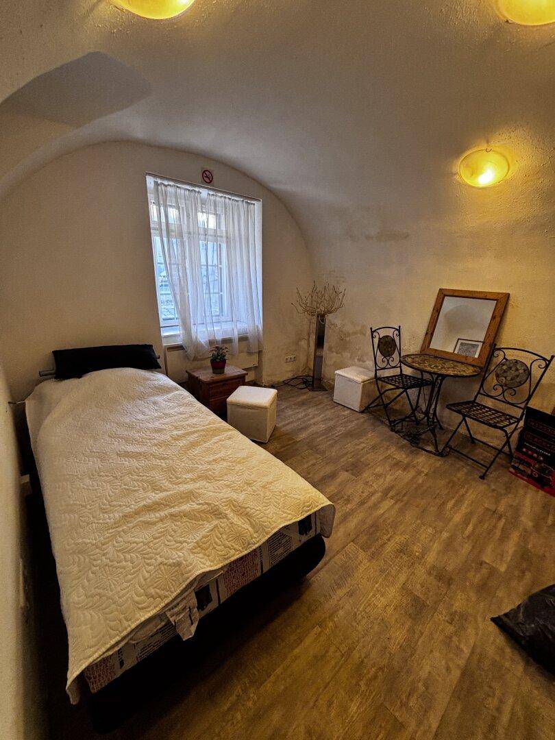 Schlafzimmer mit Einzelbett, kleinem Tisch und gewölbter Decke, hell durch das Fenster.