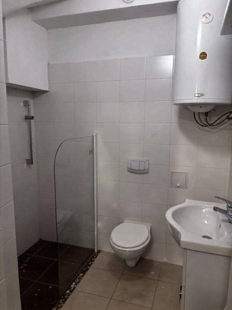 Badezimmer mit Dusche, WC, Waschbecken und einem Warmwasserboiler an der Wand.