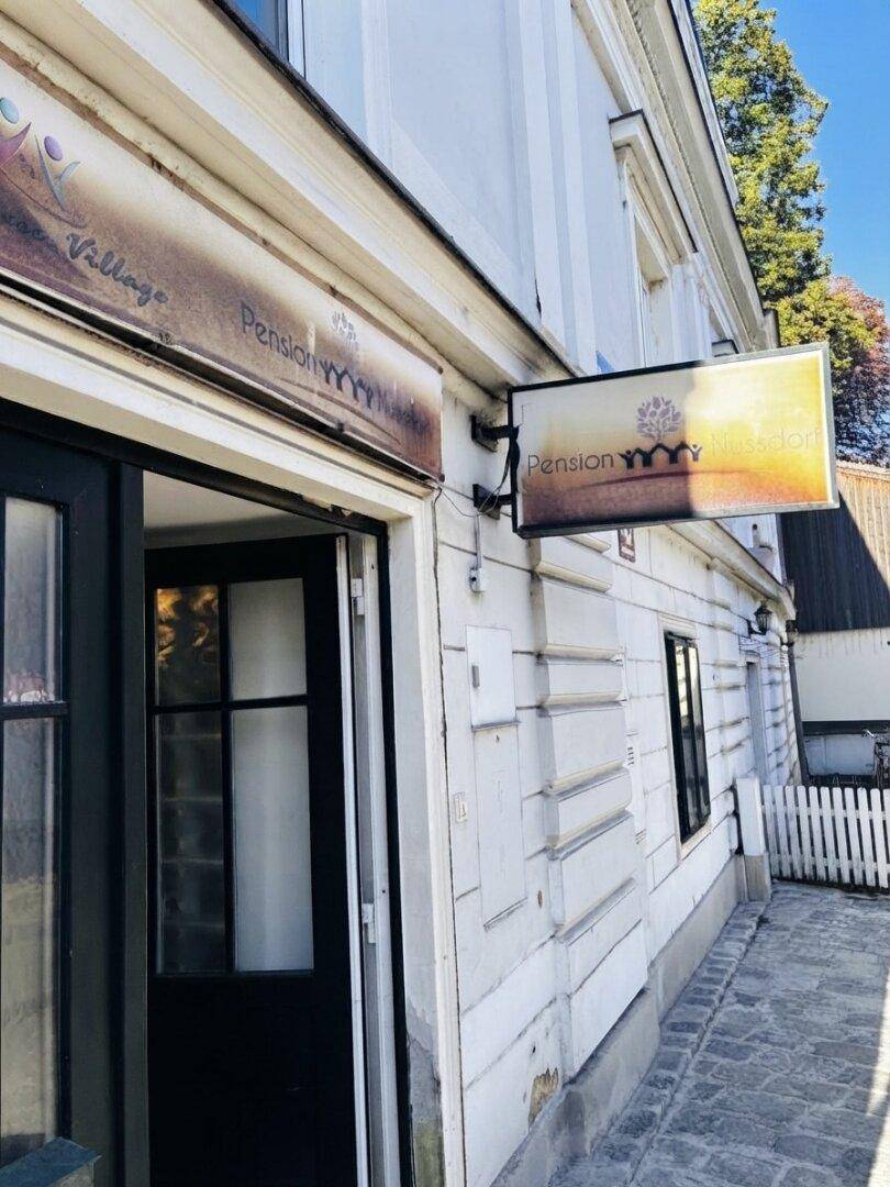 Außenansicht einer Pension mit weißer Fassade und einem Werbeschild über dem Eingang.