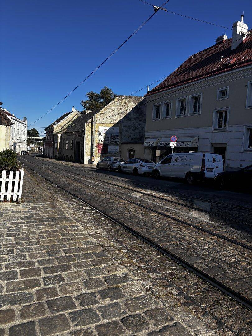 Straßenansicht mit Straßenbahnschienen, historischen Gebäuden und geparkten Autos.