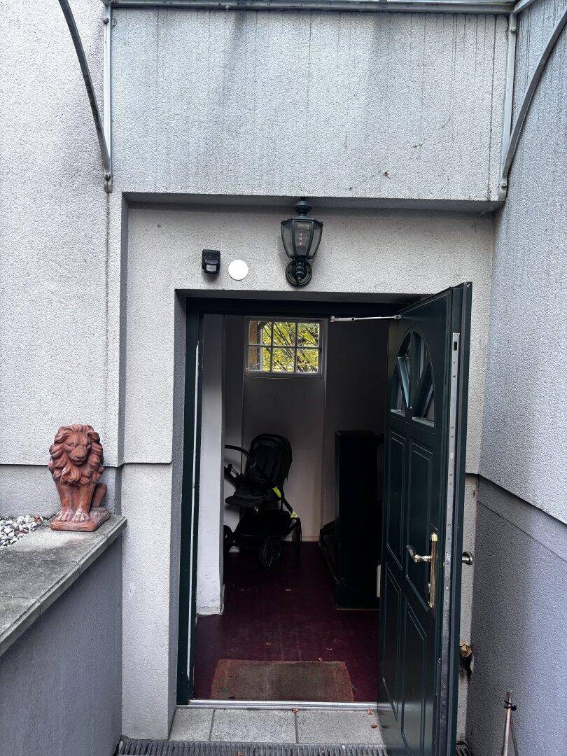 Eingangsbereich eines Gebäudes mit offener Tür und einer Löwenstatue daneben.