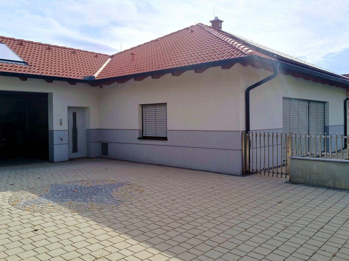 Seitenansicht des Hauses mit gepflasterter Einfahrt und geschlossenen Rollläden an den Fenstern.