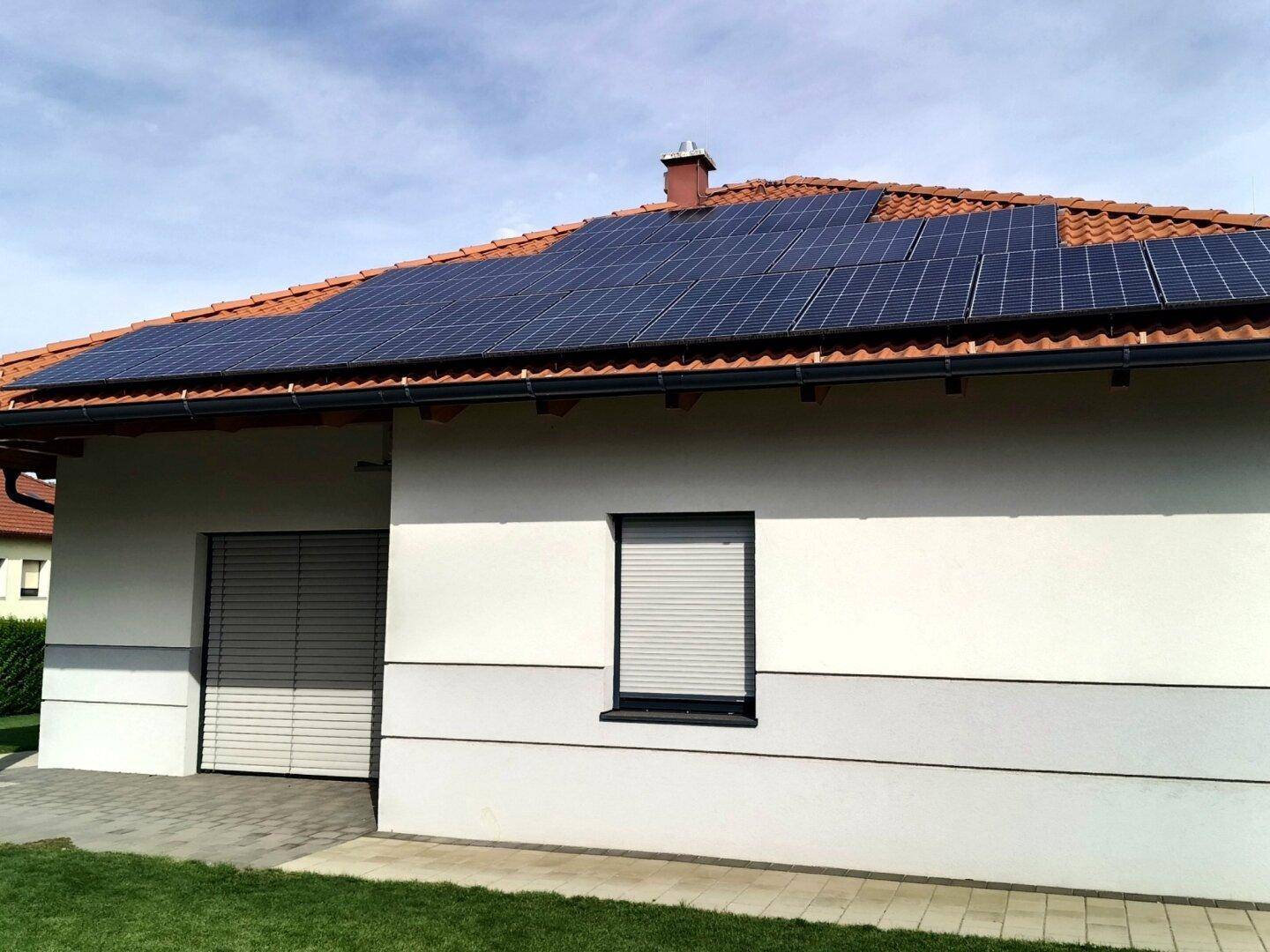 Hausfassade mit Garage, Rollläden und Photovoltaikmodulen auf dem Ziegeldach.