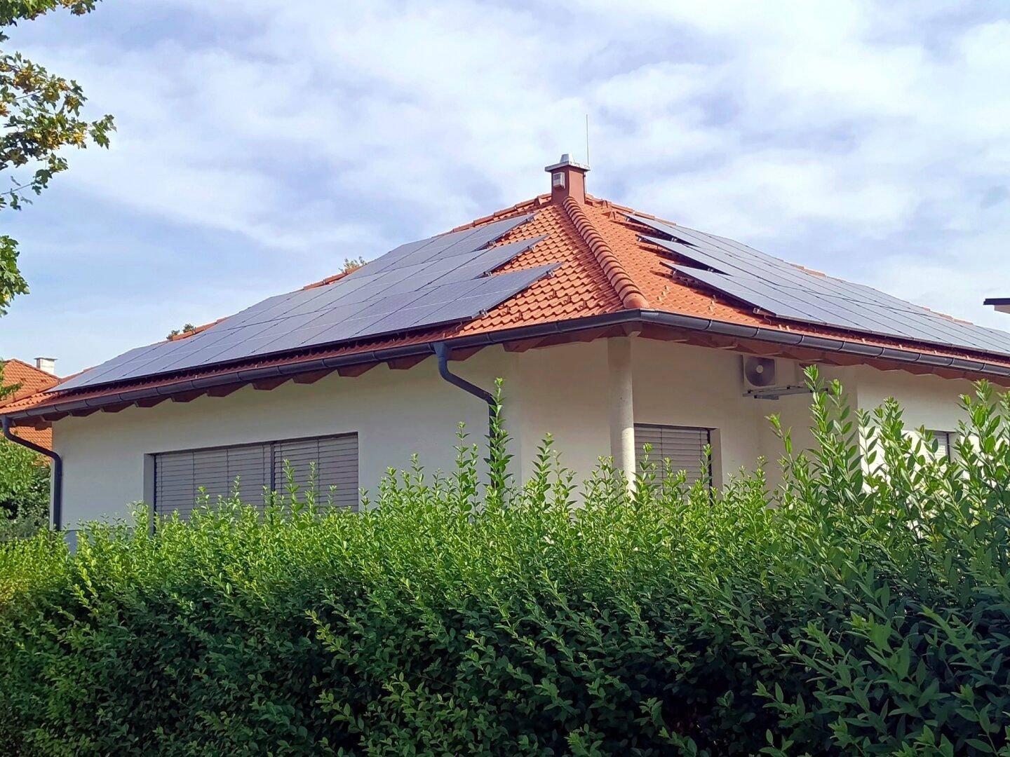 Einfamilienhaus mit Photovoltaikanlage, umgeben von einer dichten, grünen Hecke.