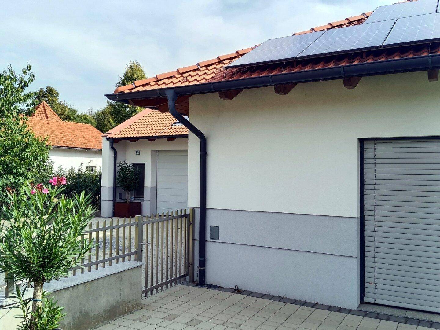 Seitenansicht des Hauses mit Regenrinne, Rollläden und einem Metallzaun.