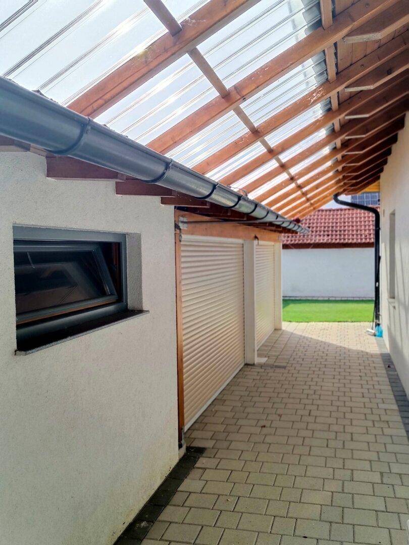 Überdachter Gang mit transparentem Dach und Rollläden an der Garagenwand.