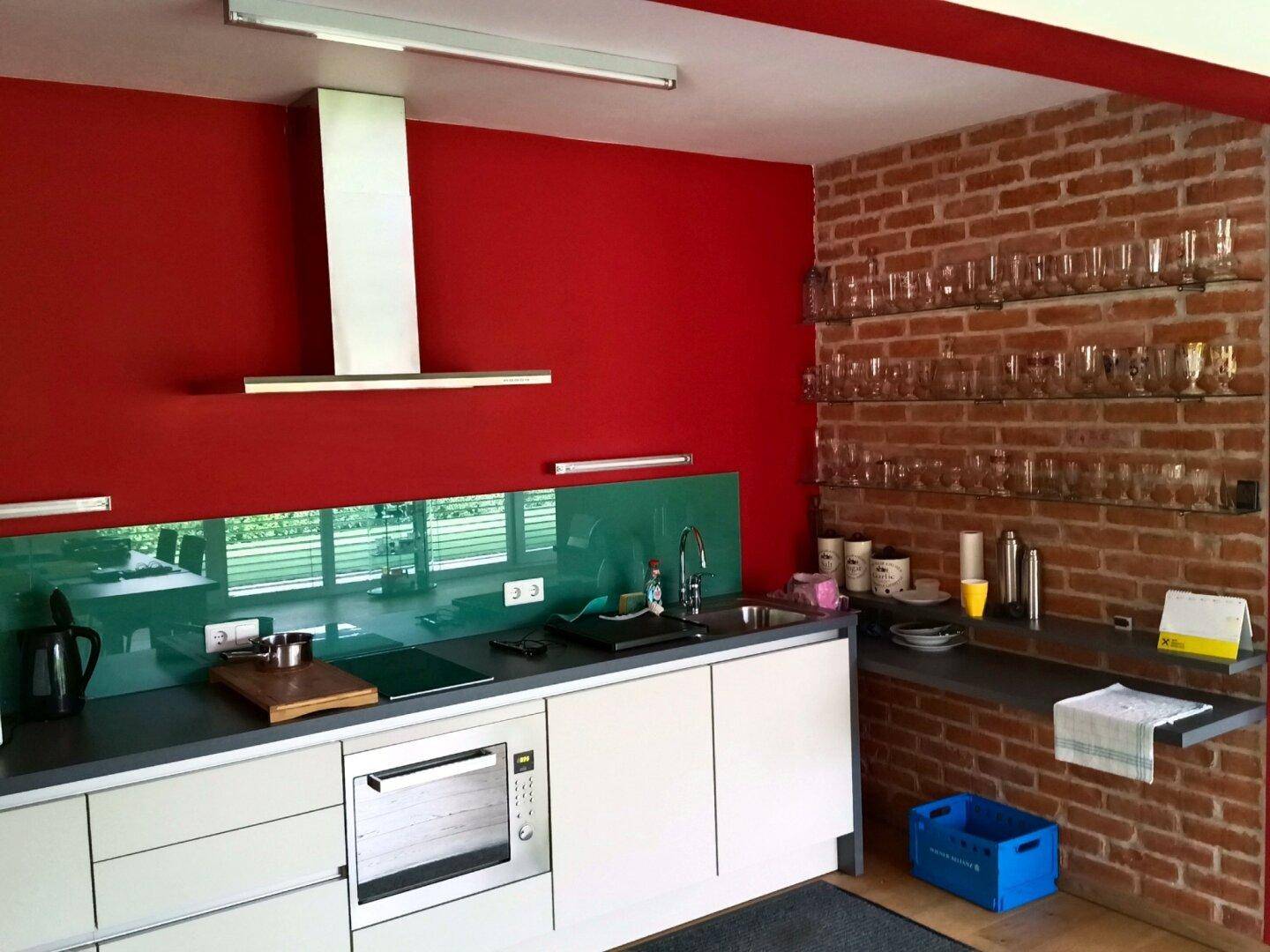 Küchenzeile mit roter Wand, Backsplash aus Glas und freiliegender Ziegelwand.