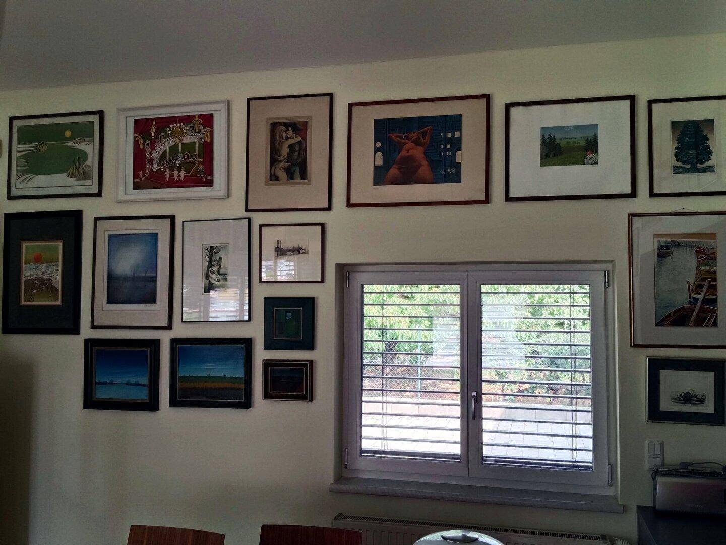 Fenster im Wohnzimmer mit Rollläden und einer Galerie von gerahmten Bildern an der Wand.
