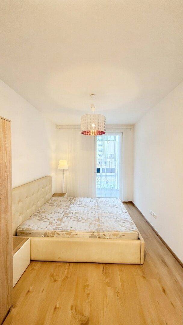 Helles Schlafzimmer mit Holzboden, einem Bett und Zugang zu einem Balkon oder einer Terrasse.