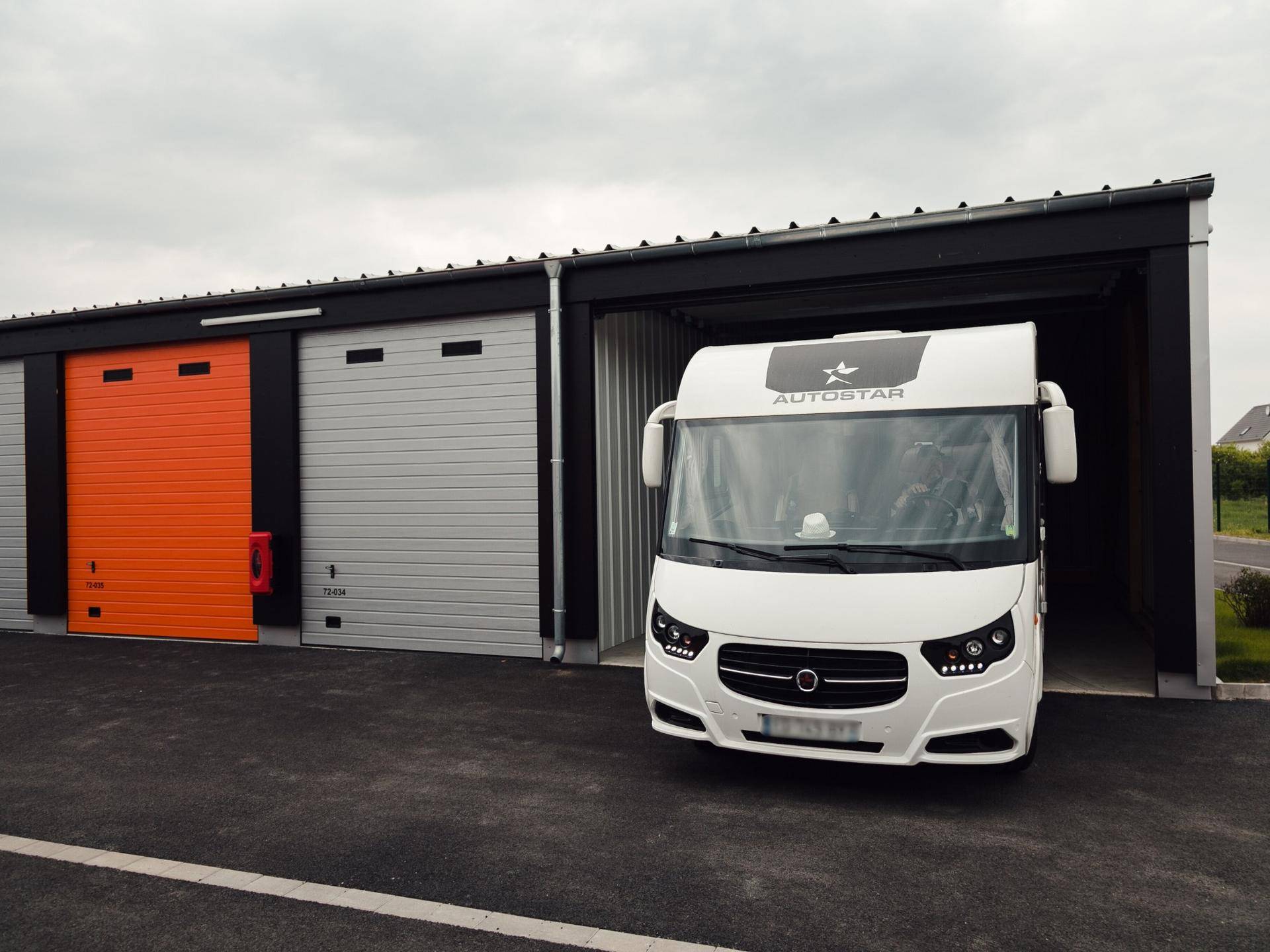 Weißer Wohnwagen parkt vor einer offenen Lagerhalle, die als Garage dient.